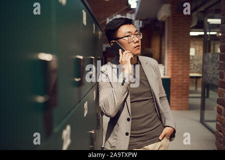 Taille bis Portrait von erfolgreiche asiatische Geschäftsmann spricht von Smartphone stehen Schließfächer in modernen Büro-, Copy space Stockfoto
