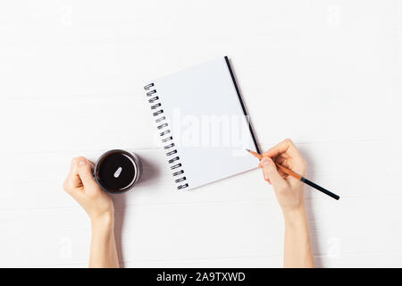Ansicht von oben weibliche Hände halten Bleistift über leeres Papier Notebook und Tasse Kaffee auf weiße Holztisch Stockfoto