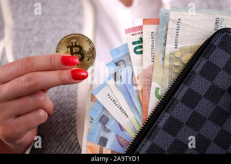 Virtuelle cryptocurrency Geld Bitcoin goldenen Münzen in der linken Hand einer Frau mit rotem Nagellack und den Geldbeutel. Die Zukunft des Geldes. Euro-banknoten. Stockfoto