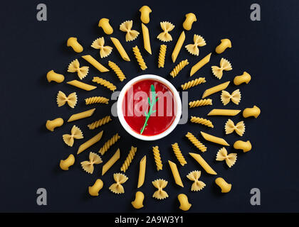 Tomaten in der Mitte der Kreis angeordneten Pasta. Andere Art von Pasta geometrische auf schwarzem Hintergrund angeordnet. Stockfoto