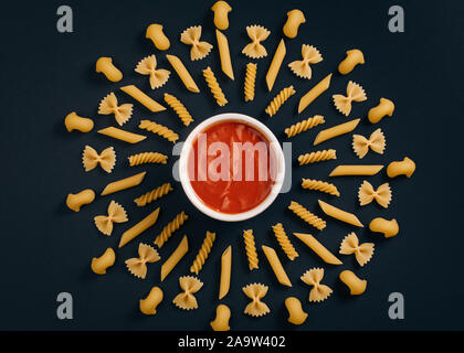 Tomaten in der Mitte der Kreis angeordneten Pasta. Andere Art von Pasta geometrische auf schwarzem Hintergrund angeordnet. Stockfoto