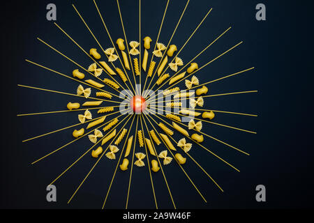 Tomaten in der Mitte der Kreis angeordneten Pasta. Andere Art von Pasta geometrische auf schwarzem Hintergrund angeordnet. Stockfoto