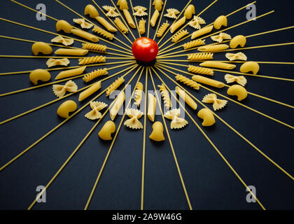 Tomaten in der Mitte der Kreis angeordneten Pasta. Andere Art von Pasta geometrische auf schwarzem Hintergrund angeordnet. Stockfoto