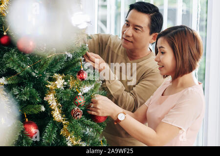 Reifer Mann und Frau schmücken Weihnachtsbaum im Wohnzimmer Stockfoto