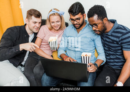 Gruppe von Freunden genießt die Zeit zusammen und suchen am Laptop. Multirassischen junge Menschen im Wohnzimmer zu Hause sitzen, Videos, po Essen Stockfoto