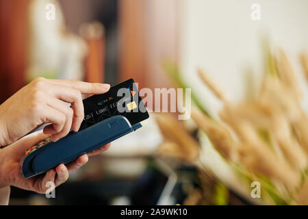 Hände von Kassierer streichen Kreditkarte durch die Klemme bei der Annahme von Zahlungen von Kunden des Auftraggebers Stockfoto