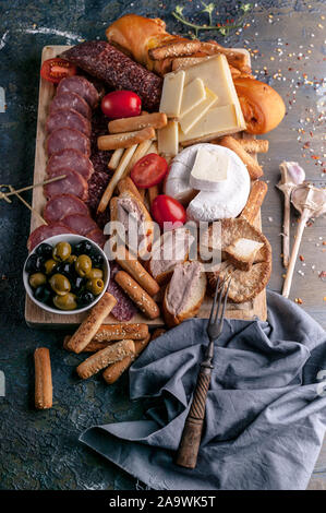 Verschiedene Käsesorten, geräucherte Fleisch- und Wurstwaren auf einem Schneidebrett. Mediterrane Speisen. Ansicht von oben. Vertikaler Dampfstoß Stockfoto