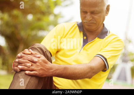 Älterer Mann mit einer Knieverletzung - Begriff älterer Mann fitness und yoga im Freien - Selektive focucs an Hand, alten Mann mit Knie aufgrund von Schmerzen. Stockfoto