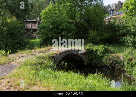 Ponte Ferreira Römische Brücke über den Río de Ferreira in Ferreira, Spanien. In der Ferne ist ein typisch galizischen Getreidespeicher bekannt als ein Hórreo. Die vil