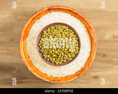 Reis und mung Bean in der Schüssel und Lehm Platte auf braunem Holz- Hintergrund. Indische Küche, Ayurveda, Naturheilkunde, moderne Apotheke Konzept Stockfoto