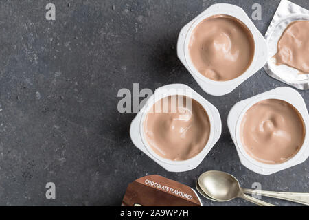 Schokolade Joghurtbecher auf Schwarz gesprenkelter Hintergrund mit kleinen silbernen Löffel - Drei mit Schokoladegeschmack Joghurtbecher mit Folie Deckel Stockfoto