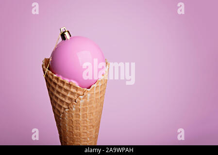 Christmas Ball bemalt hellrosa Farbe in Eis Waffel Kegel auf rosa Hintergrund. Stockfoto