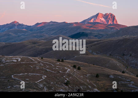 Berg Corno Grande am Horizont hinter kargen und ländliche Landschaft leuchtendem Pink im Licht des Sonnenaufgangs, Abruzzen, Italien Stockfoto