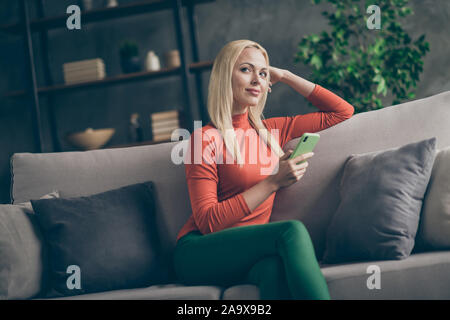 Foto der hübschen blonden Dame heimische Stimmung holding Telefon Phantasie Flug denken über neue kreative post Text sitting Comfy couch casual Outfit Stockfoto