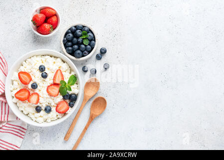 Quark, Hüttenkäse oder tvorog oder Ricotta mit frischen Beeren in Schüssel auf konkreten Hintergrund. Gesundes Milchprodukt, Quelle des Kalziums und Protein Stockfoto