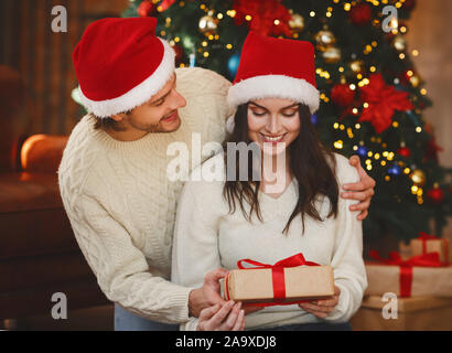 Fröhlicher Mann in Santa hat Gruß Frau mit Weihnachtsgeschenk Stockfoto