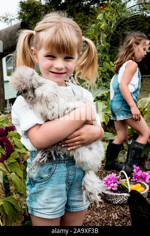 Blonde Mädchen stehen in einem Garten, flauschig grau Huhn. Stockfoto