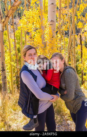 Eine reife Frau, Junge und Mädchen, eine Mutter und ihre zwei Kinder in Wäldern, Aspen Bäume im Herbst Farbe, Stockfoto