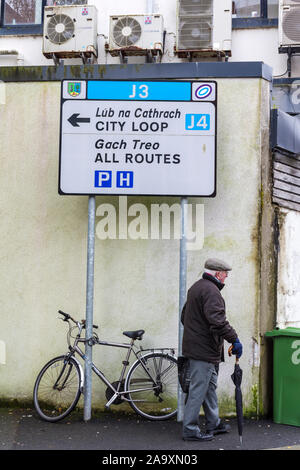 Älterer Mann mit Regenschirm Spaziergänge in der Stadt durch die Anmeldung in Gälisch Irisch und Englisch Sprache. Sligo, County Sligo, Irland Stockfoto
