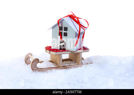 Haus mit einem roten Band auf einem Schlitten. Winter Verkauf von Immobilien. Stockfoto