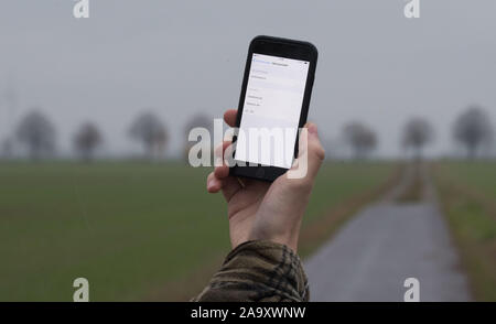 Hemmingen, Deutschland. Nov, 2019 18. Abbildung - ein Mann in der Region Hannover lässt sein Smartphone suchen für Netzbetreiber auf einem Feld Pfad (inszenierte Szene). Die Bundesregierung will sich grundlegend in Deutschland Internet und Handy Empfang in den nächsten zwei Jahren verbessern. Credit: Julian Stratenschulte/dpa/Alamy leben Nachrichten Stockfoto