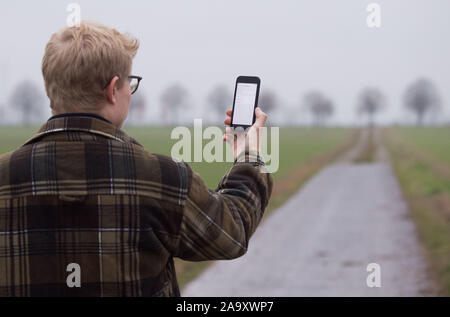 Hemmingen, Deutschland. Nov, 2019 18. Abbildung - ein Mann in der Region Hannover lässt sein Smartphone suchen für Netzbetreiber auf einem Feld Pfad (inszenierte Szene). Die Bundesregierung will sich grundlegend in Deutschland Internet und Handy Empfang in den nächsten zwei Jahren verbessern. Credit: Julian Stratenschulte/dpa/Alamy leben Nachrichten Stockfoto