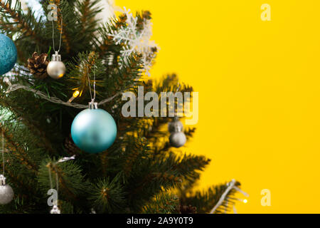Schönen grünen Weihnachtsbaum mit Kugeln und Girlanden dekoriert. Nahaufnahme. Gelber Hintergrund Stockfoto