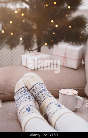 Frau in lustige Weihnachtssocken sitzen in der Nähe von Tree mit Geschenken Stockfoto
