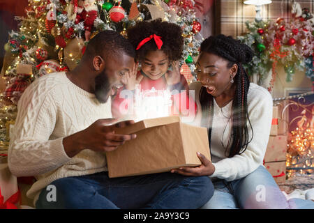 Aufgeregt schwarze Familie von drei Eröffnung scheint Weihnachten Geschenkverpackung Stockfoto