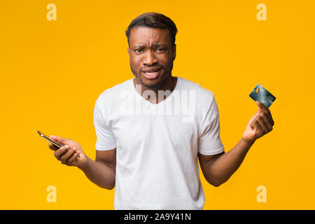 Verwirrt Guy Holding Smartphone und Kreditkarte posiert im Studio Stockfoto