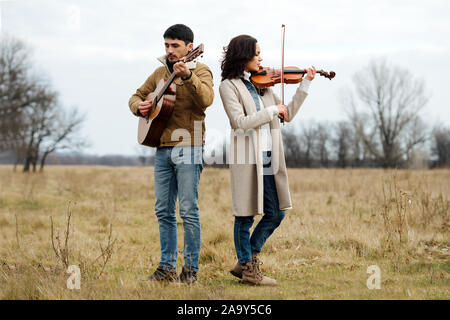 Geiger und Gitarristen spielen Musik in der Mitte der anl Herbst Feld aus Gras Stockfoto