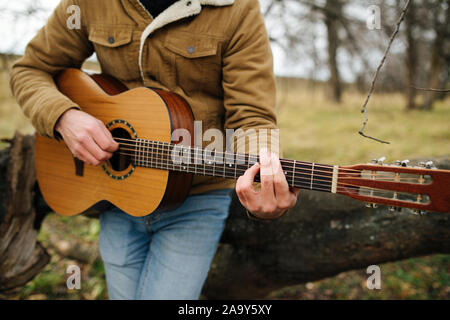 7/8-Foto von einem Warm gekleideten Mann spielt Gitarre in einer Landschaft Stockfoto