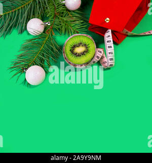 Konzept Weihnachtsferien Diät und healhty Lebensstil - Kiwi und Maßband mit rot Geschenkbeutel und grünen Tannenbaum Äste am trendigen grün blau Hintergrund. Flach, Ansicht von oben, kopieren. Stockfoto