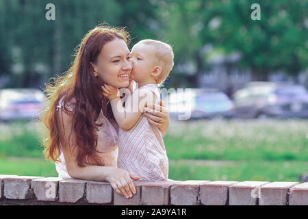 Kleines Mädchen küsst sie Mama beim Spaziergang im Park Stockfoto