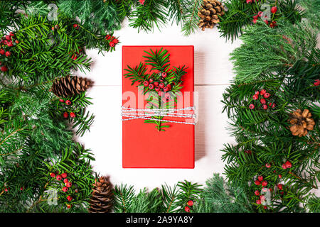 Weihnachten rot Geschenkbox und Tannenbaum Äste mit Beeren auf weißem Hintergrund, isoliert. Dezember, winter Zusammensetzung. Flach, Ansicht von oben auf das Neue Jahr Layout. Platz für Text. Rahmen für Urlaub Layout. Stockfoto
