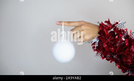 Fake Schneeball hängt vom Finger einer Frau. Woman's Hand gewickelt mit dekorativen Silvester Girlanden. Kopieren Sie Platz für Werbung. Negativer Platz. Stockfoto
