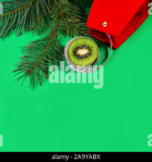 Konzept Weihnachtsferien Diät und healhty Lebensstil - Kiwi und Maßband mit rot Geschenkbeutel und grünen Tannenbaum Äste am trendigen grün blau Hintergrund. Flach, Ansicht von oben, kopieren. Stockfoto