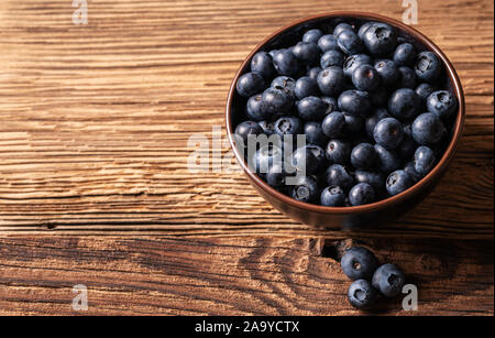 Frische reife Heidelbeeren in braun Keramik Schüssel auf Holz- Hintergrund, Zutaten für gesunde Ernährung lifestyle Konzept, 45 Grad Winkel betrachten, horizontal Stockfoto