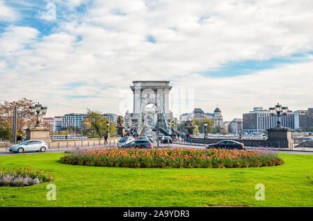 Budapest, Ungarn - Nov 6, 2019: Széchenyi Kettenbrücke in Budapest mit den angrenzenden Kreisverkehr, die zu den berühmten Wahrzeichen fotografiert. Autos, Verkehr. Gras und Blumen im Vordergrund. Stockfoto