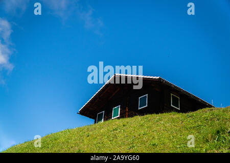 Ein Ferienhaus aus Holz auf dem Gipfel des Berges auf blauen Himmel Hintergrund isoliert - österreichische Landschaft an einem schönen sonnigen Tag in den Bergen Stockfoto