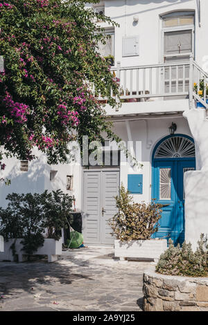 Fassade eines typischen Mykonischen weißes Haus mit blauen Tür rosa blühenden Baum vor, Mykonos, Griechenland. Stockfoto