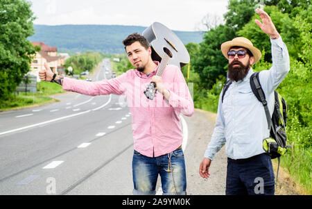 Anreise per Autostop. Hoffnungslos hitchhiker. Unternehmen Freunde auf der Suche nach transportieren. Männer versuchen stop Auto. Reisende mit Rucksack und Gitarre bereit Strat neue Reise. Hitchhiker treffen Freund an der Straße. Stockfoto