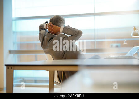 Rückansicht Blickrichtung der Geschäftsmann im Büro Stuhl gelehnt mit Arme hinter Kopf Stockfoto