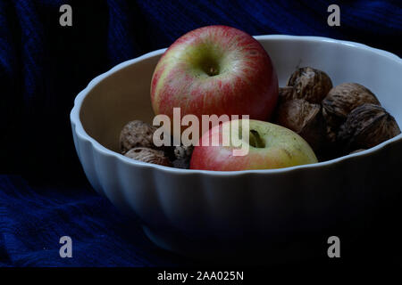 Apple und ganze Walnüsse in eine weiße Schale vor einem schwarzen Hintergrund Stockfoto