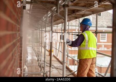 Eine Person, die das Tragen von Schutzausrüstung und stehen auf einem Gerüst, verwendet eine Spritzpistole während der Arbeit an der Außenseite von Gilman Hall, an einem kalten Tag an der Johns Hopkins Universität, Baltimore, Maryland, 11. März 2009. Vom Homewood Sammlung Fotografie. () Stockfoto