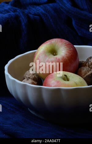 Apple und ganze Walnüsse in eine weiße Schale vor einem schwarzen Hintergrund Stockfoto