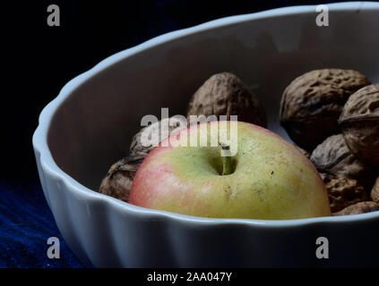 Apple und ganze Walnüsse in eine weiße Schale vor einem schwarzen Hintergrund Stockfoto