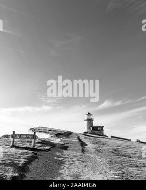 Ein Leuchtturm liegt am Rande der Kreidefelsen von Beachy Head mit einem niedrigen Sonne hebt die weiße Oberfläche thront. Ein Pfad ist im Vordergrund und Stockfoto