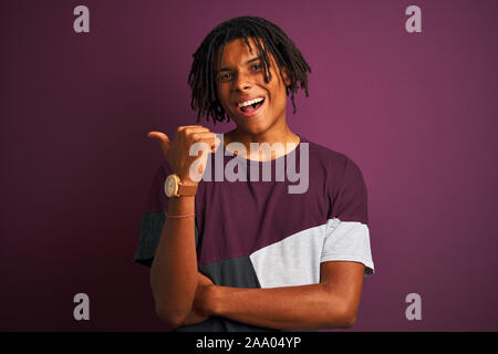 Afro Mann mit Dreadlocks tragen casual t-shirt stehend über isolierte lila Hintergrund lächelnd mit glücklichen Gesicht und mit Verweis auf die Seite Stockfoto