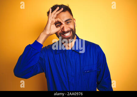 Hübscher indischer Arbeitnehmer Mann in Uniform über isolierte gelben Hintergrund tun ok Geste mit der Hand lächelnd, Auge schauen durch die Finger mit Happy Stockfoto